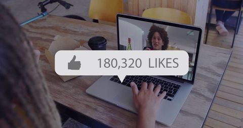 Laptop livestream engagement overlay showing 180,320 likes at casual cafe workspace