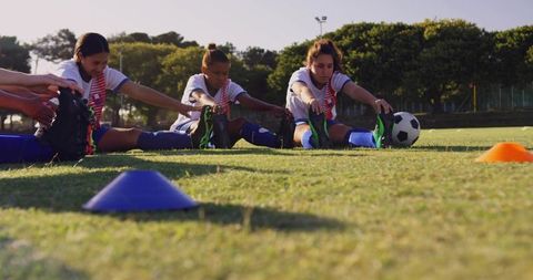 Young Female Soccer Players Stretching Before Game on Grass Field