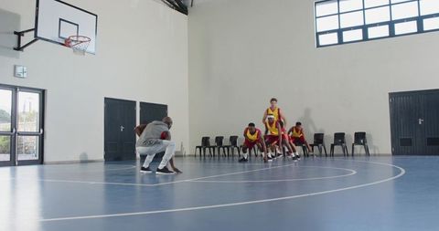 Basketball coach and team practicing defense on indoor court