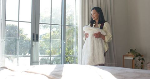 Mother Cradling Baby Near Sunlit Sliding Doors in Cozy Bedroom