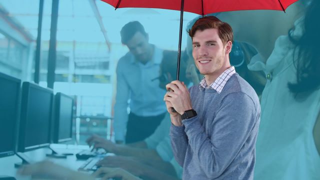 Businessman smiling while holding red umbrella in professional office environment with colleagues in the background. Ideal for themes of business protection, workplace motivation, teamwork, and modern office setups.