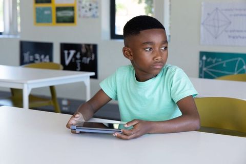 African american schoolboy holding tablet in classroom looking thoughtful and focused