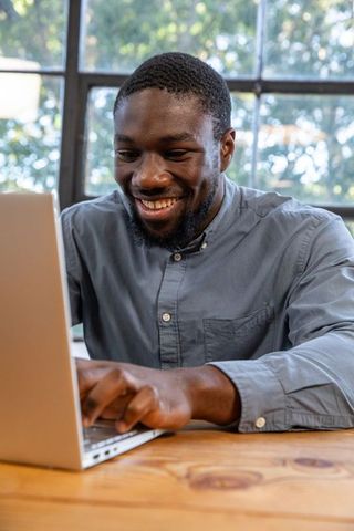 Focused African American Professional Typing on Laptop at Wooden Desk