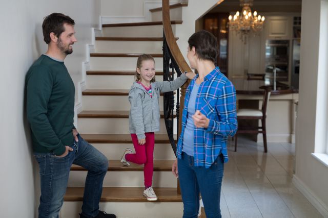 This image shows a family of three, including parents and their daughter, interacting on a staircase inside their home. The casual setting and warm interaction make it suitable for use in advertisements, family-oriented content, home decor promotions, and lifestyle blogs.