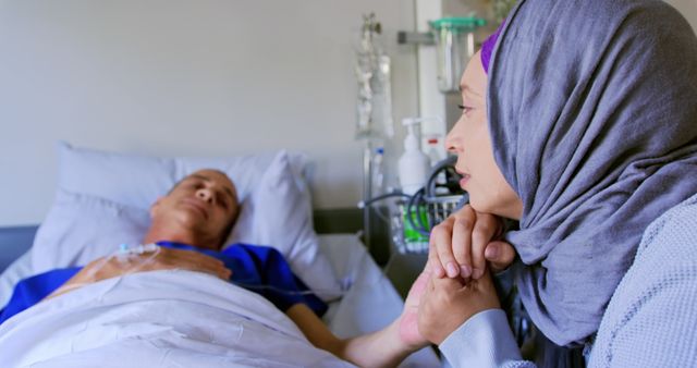 Image depicts a woman in a hijab attentively sitting at the bedside of a hospitalized family member. The curated setting emphasizes the emotional connection, support, and family care in a medical environment. This image can be used for articles or advertisements related to healthcare, patient support, emotional well-being, or family concerns during illness.