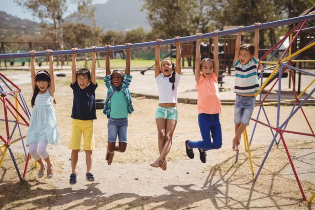 Happy schoolkids hanging on monkey bar at school playground
