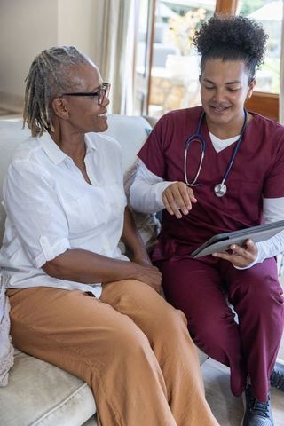 Home care nurse consulting senior african american woman using tablet for telehealth