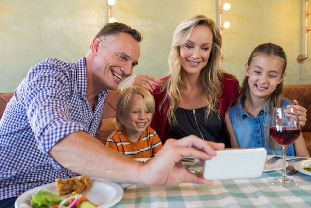 Father taking selfie with family while sitting at restaurant