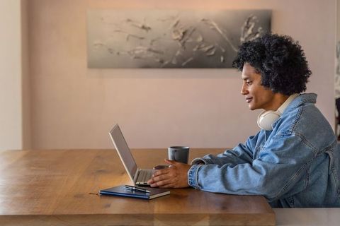 African american man working on laptop at wooden table with headphones and coffee mug