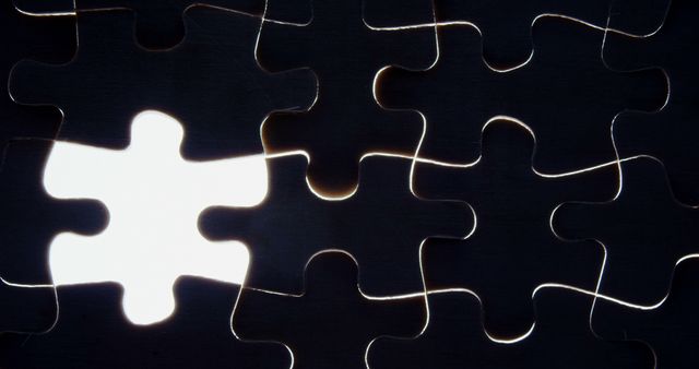 A missing puzzle piece creates a distinct contrast against the assembled black jigsaw pieces, with copy space. It symbolizes the concept of a missing element or an unsolved mystery.