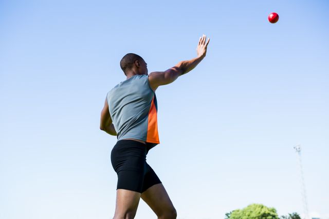 This image captures a male athlete in the midst of throwing a shot put ball during a competition in a stadium. Ideal for use in sports-related articles, fitness blogs, athletic training programs, and promotional materials for track and field events.