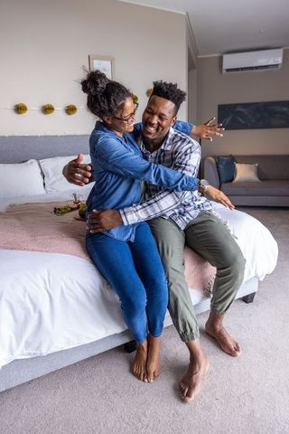 African american couple sitting on bed sharing grapes laughing in cozy intimate bedroom