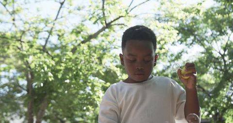 Child concentrating on bubble wand under leafy canopy playing with bubbles in sunlight