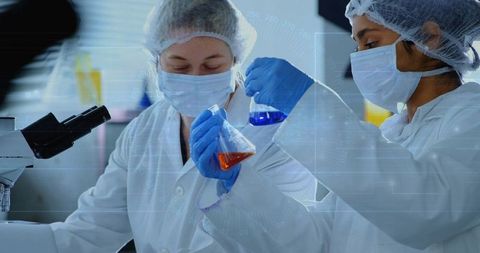 Female Scientists Collaborating in Laboratory Mixing Orange and Blue Chemicals for Research