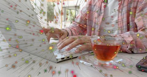 Typing on laptop with tea cup and colorful digital particle burst, remote work inspiration