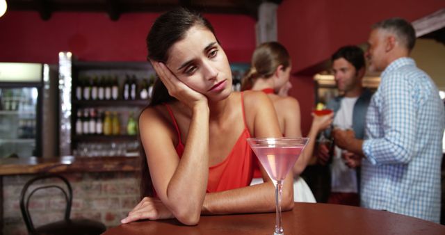 Sad woman sitting in bar while friends interacting in background