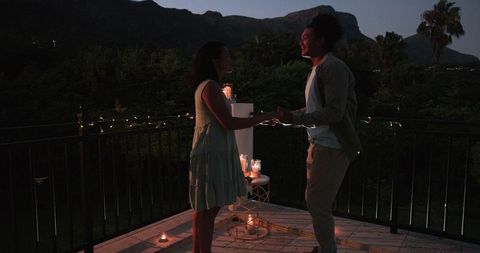 Romantic night proposal on balcony surrounded by candlelight