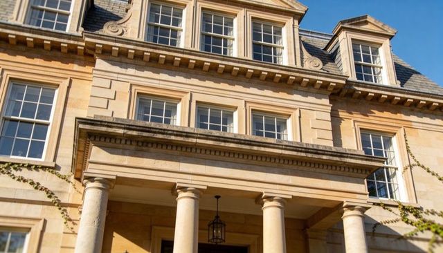 Neoclassical manor entrance with four columns, dentil cornice, hanging lantern, sunlit ivy
