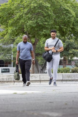 African american men walking with gym duffel bags on city sidewalk under tree canopy