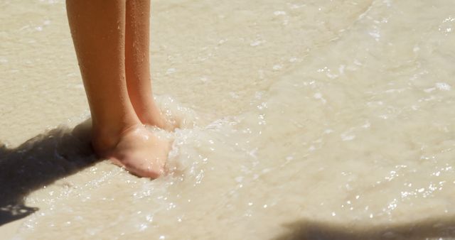 Legs of caucasian girl standing in water on sunny beach. Childhood, free time, summer, travel, vacations and lifestyle, unaltered.