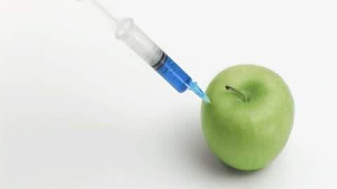 Syringe Injecting Liquid into Green Apple in Slow Motion