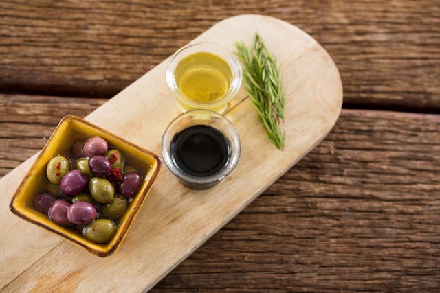 Close-up of marinated olive, rosemary with olive oil and balsamic vinegar on wooden tray