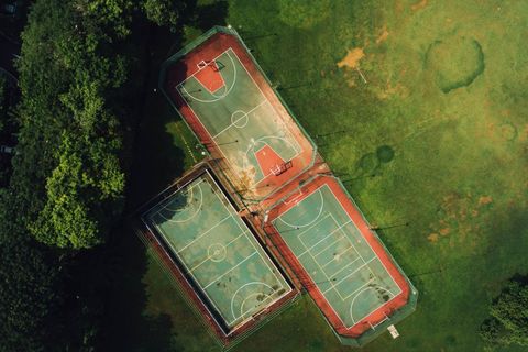 Overhead view showing three outdoor basketball and tennis courts surrounded by green park