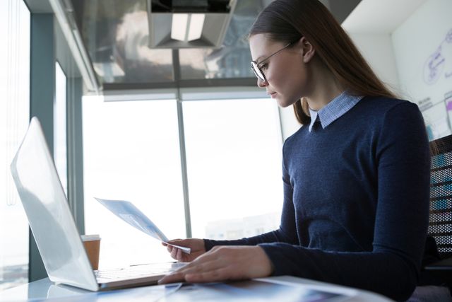 Female executive looking at document wile using laptop in office