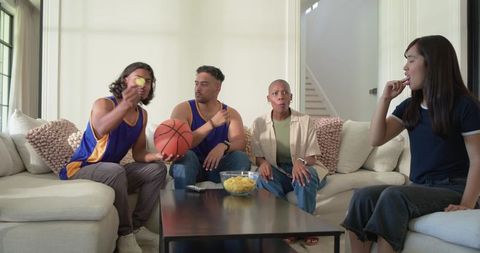 Friends watching basketball game at home on couch wearing jerseys while snacking