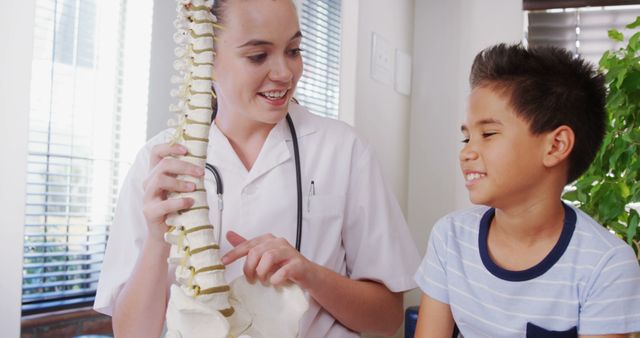 Medical professional wearing white coat demonstrating a spine anatomy model to a young boy who is smiling. This image is suitable for use in pediatric care, health education, medical consultations, healthcare advertisements, pediatrician promotions, and educational materials on human anatomy and child healthcare.