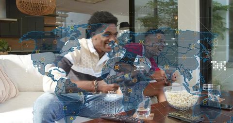 Friends gaming together on couch in modern living room with popcorn and global data overlay