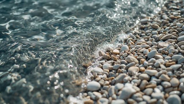 Lapping seawater on smooth pebble shore with sparkling ripples and coastal texture