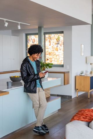 African american man leaning on blue kitchen island checking smartphone in minimalist home