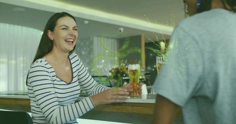 Laughing woman holding pilsner glass at modern lounge bar with friends, beer splash
