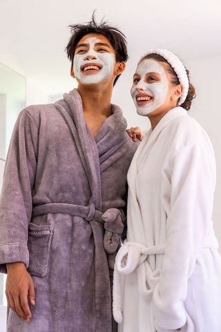 Multicultural couple enjoying home spa night wearing facial masks and plush bathrobes