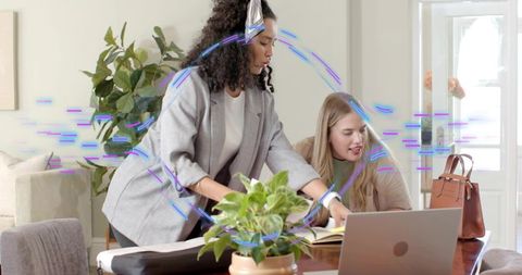 Women collaborating at home desk pointing at notes while working on laptop casual teamwork