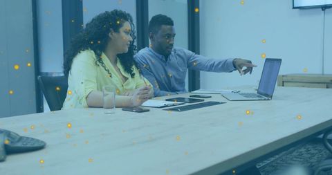 Team collaborating over laptop while man pointing and woman listening in boardroom