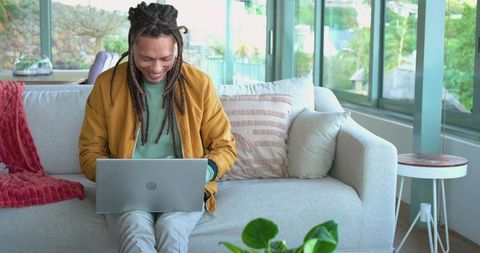 Mid adult african american man working on laptop in sunlit modern living room with plants
