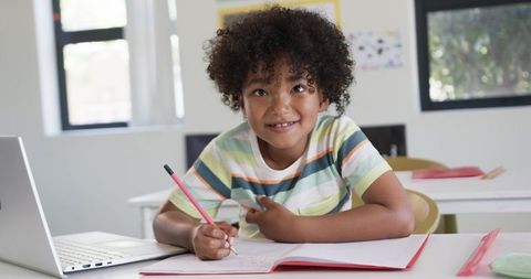 African American Child Writing and Learning with Laptop in Bright Classroom