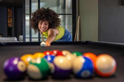 African american woman lining up shot on pool table smiling in stylish home game room