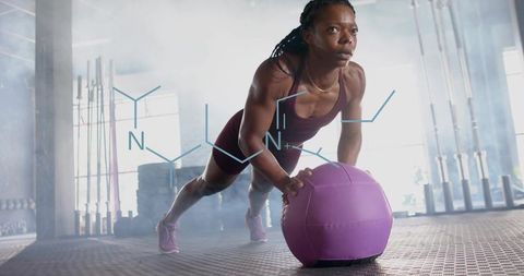 Female athlete pushing purple medicine ball in gym for intense core strength training
