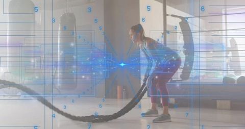 Female athlete training with battle ropes and futuristic digital overlay in gym for fitness