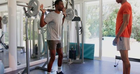 Young Man Lifting Weights with Supportive Friend in Modern Gym