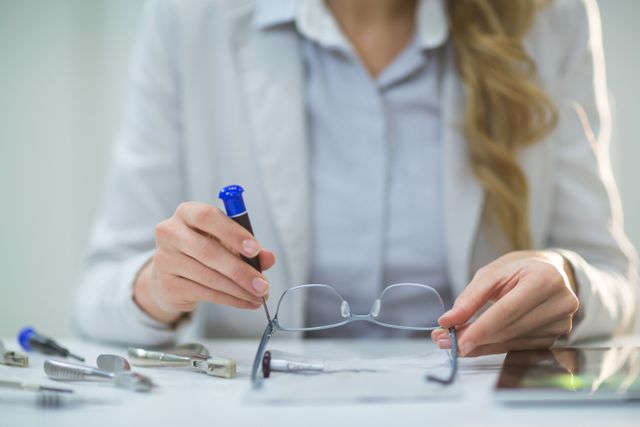 Female optometrist adjusting eyeglass frame with precision tools in a clinic. Ideal for use in articles or advertisements related to eye care, optometry services, vision health, and professional healthcare settings.
