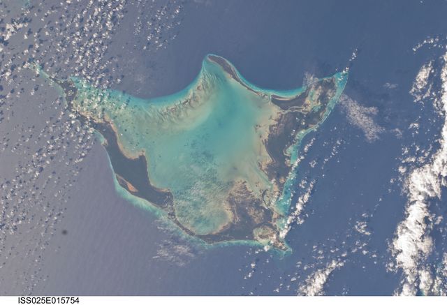 Aerial view of Acklins Island captured from the International Space Station. The island's unique horseshoe-shaped formation is clearly visible surrounded by blue ocean waters. This can be used for educational content about geography, specific showcases of the Bahamas, articles on space exploration, environmental studies, travel guides, and nature conservation topics.