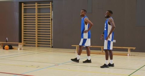 Two basketball teammates chatting on indoor court wearing blue and white jerseys