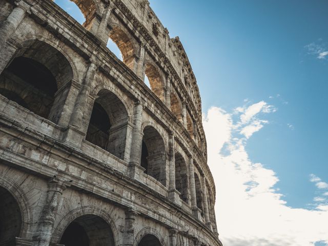 Photograph features a majestic view of the ancient Roman Colosseum against a clear blue sky. It offers a glimpse into detailed ancient Roman architecture and is ideal for tourism campaigns, educational materials on ancient history, travel magazines, cultural posters, and architectural studies.