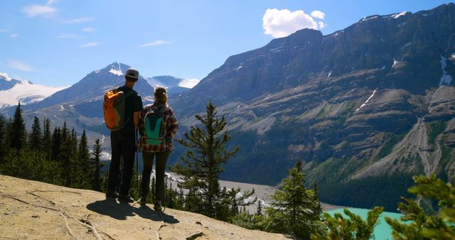 Caucasian tourist couple standing on cliff and looking at mountains by sunny lake - Download Free Stock Photos Pikwizard.com