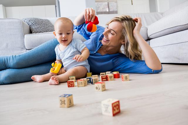 Mother looking at baby boy playing with toys in living room at home
