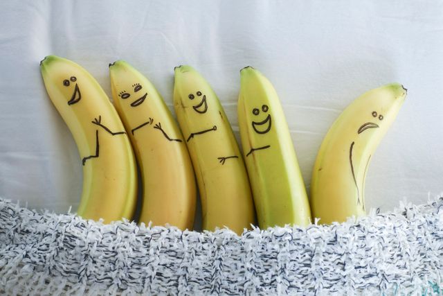 Creative arrangement of five bananas with hand-drawn smiley faces tucked under a blanket. Great for promoting fun, creativity, and food art, or for use in playful and whimsical marketing campaigns.